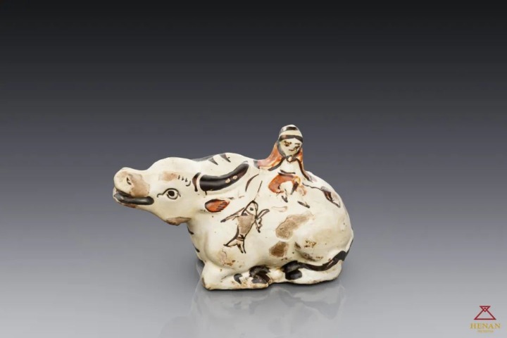 Painted white-glazed ceramic sculpture depicting a boy riding a buffalo